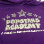 A silver and Crystal Logo on a purple hoodie for Popstars Dance Academy
